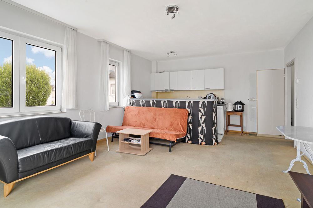 Helles Wohnzimmer mit schwarzem Sofa, orangem Sofa, Couchtisch und offener Küche.