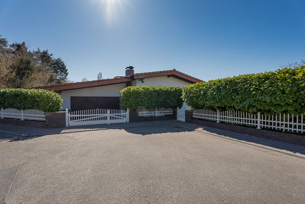 Einfamilienhaus mit rotem Dach, weißem Zaun und grünen Hecken vor dem Haus.