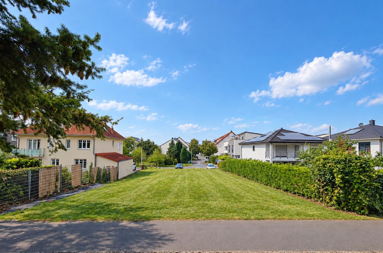 Grüner Garten mit Rasenfläche, umgeben von Wohnhäusern und Büschen unter blauem Himmel.