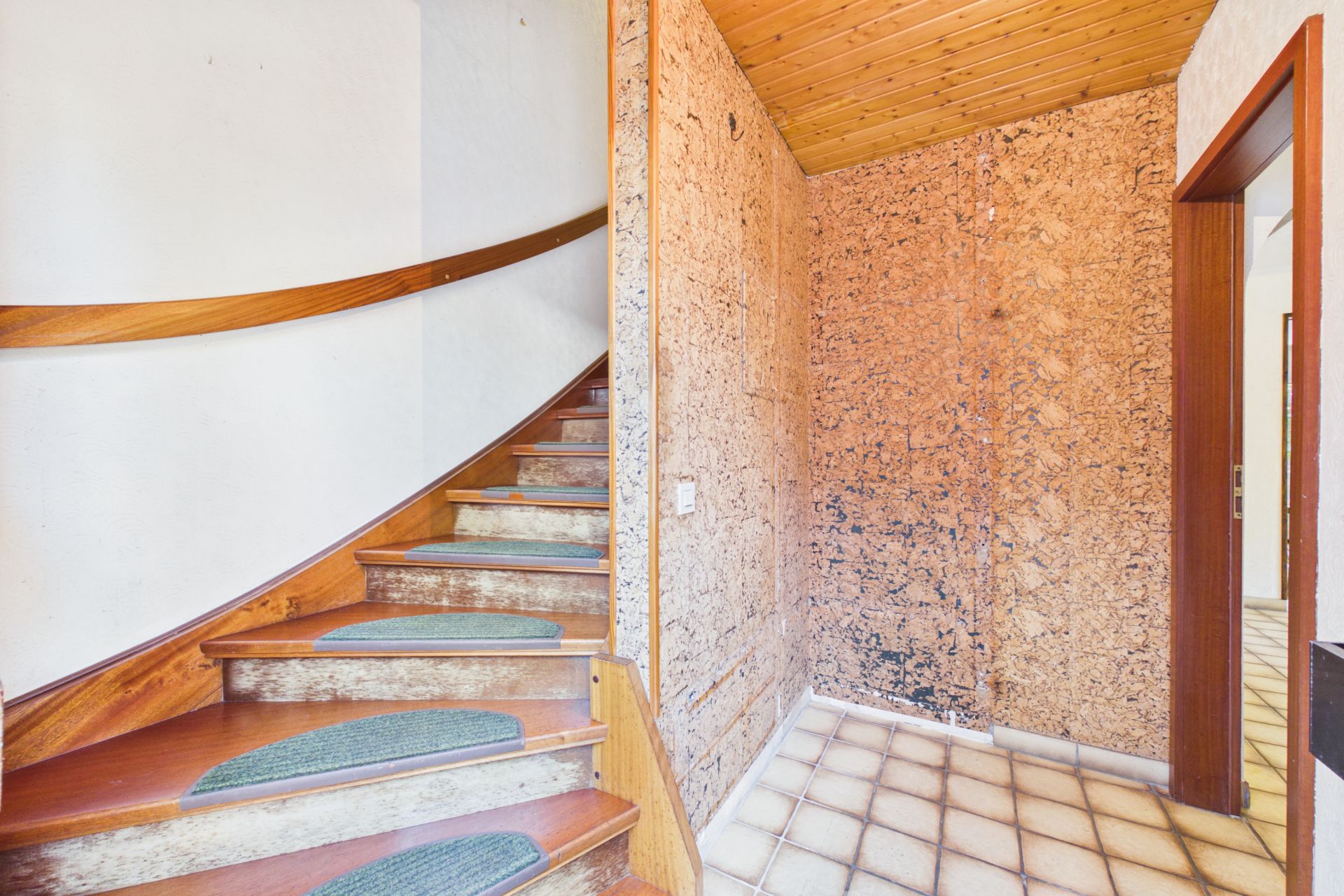 Flur mit Holztreppe, Korkwand und gefliestem Boden in einem Wohnhaus.
