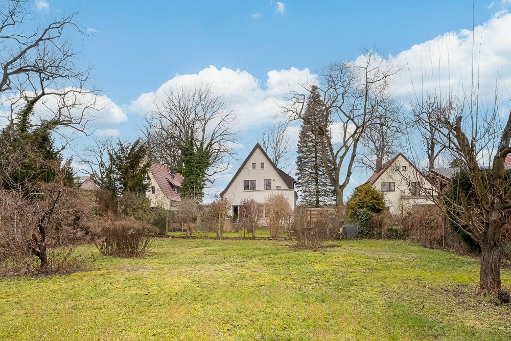 Großer Garten mit Rasenfläche und mehreren Einfamilienhäusern im Hintergrund.