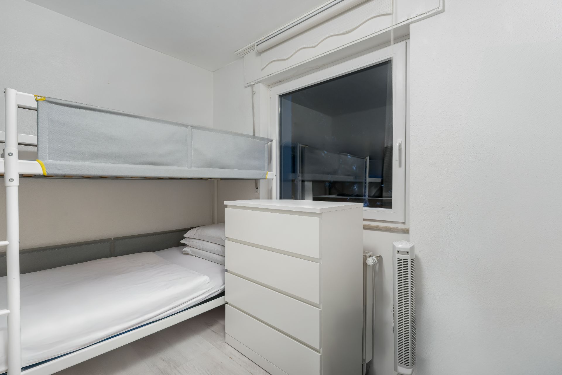 Kinderzimmer mit Etagenbett, weißer Kommode und Fenster.