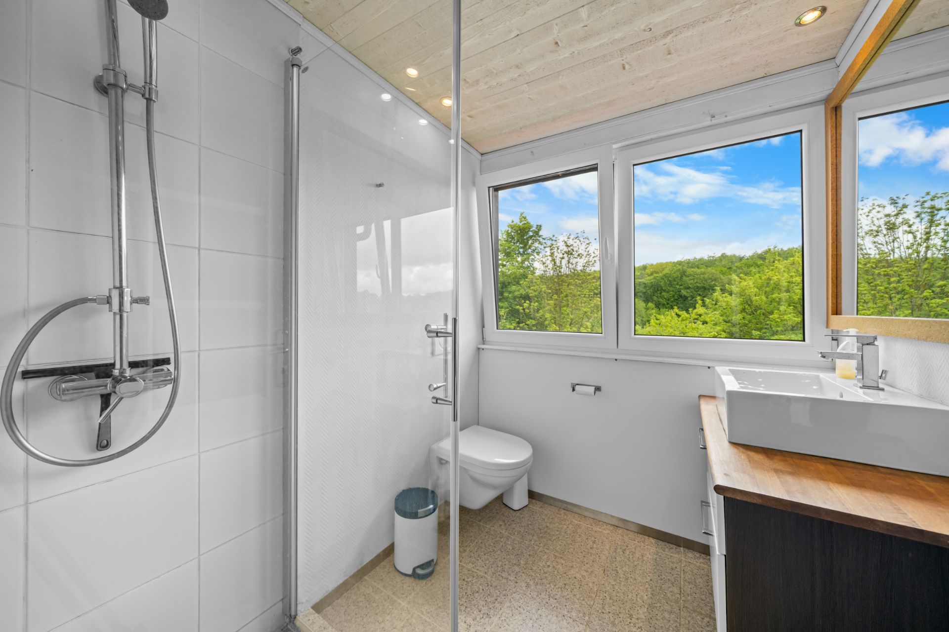 Modernes Badezimmer mit Dusche, WC, Waschbecken und großen Fenstern mit Blick ins Grüne.