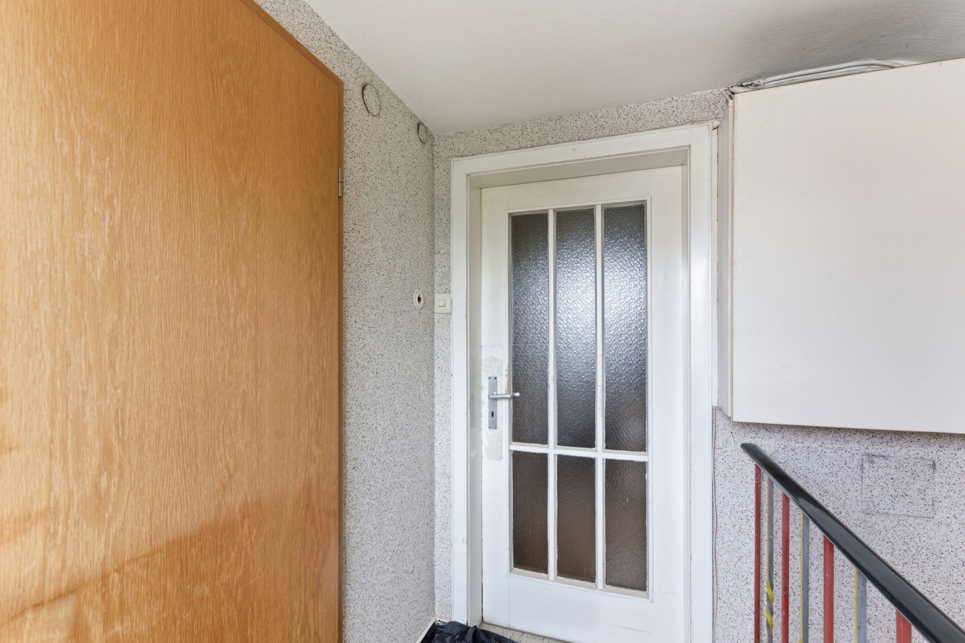 Eingangsbereich mit weißer Tür, Holztür und Treppengeländer.