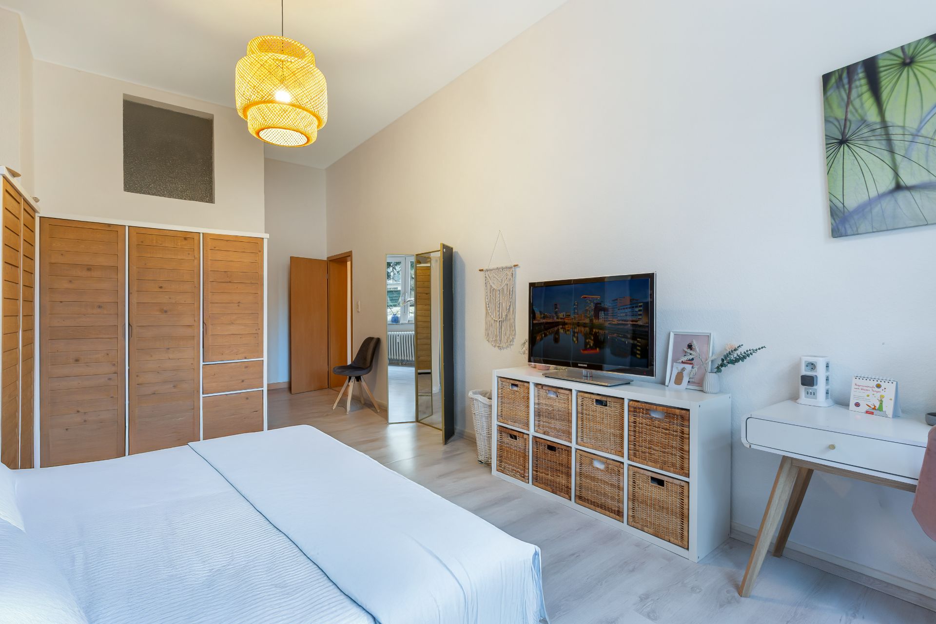 Helles Schlafzimmer mit Holzmöbeln, einem Fernseher, Schreibtisch und Dekoration an der Wand.