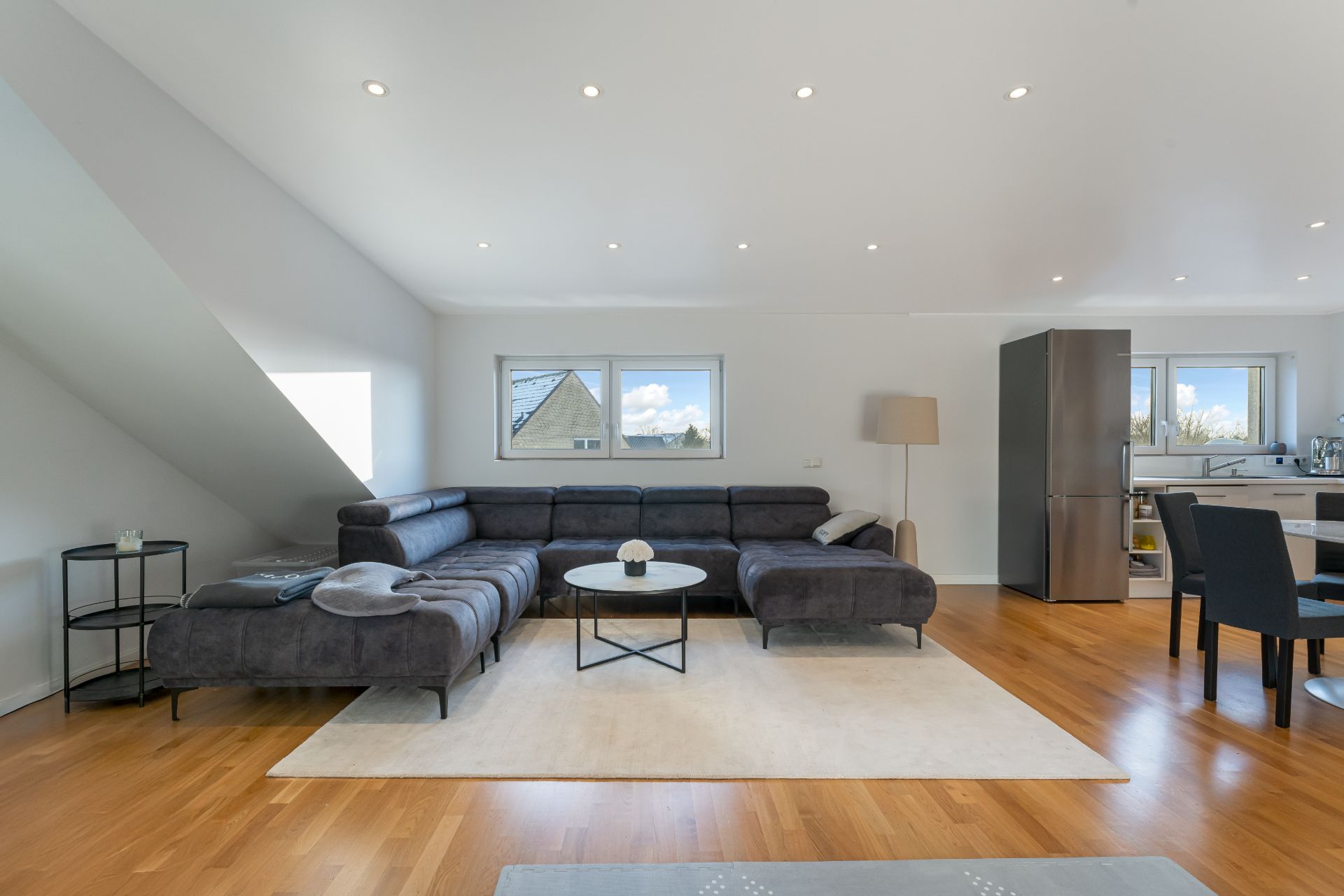 Modernes Wohnzimmer mit Ecksofa, Couchtisch, Stehlampe und offener Küche auf Holzfußboden.
