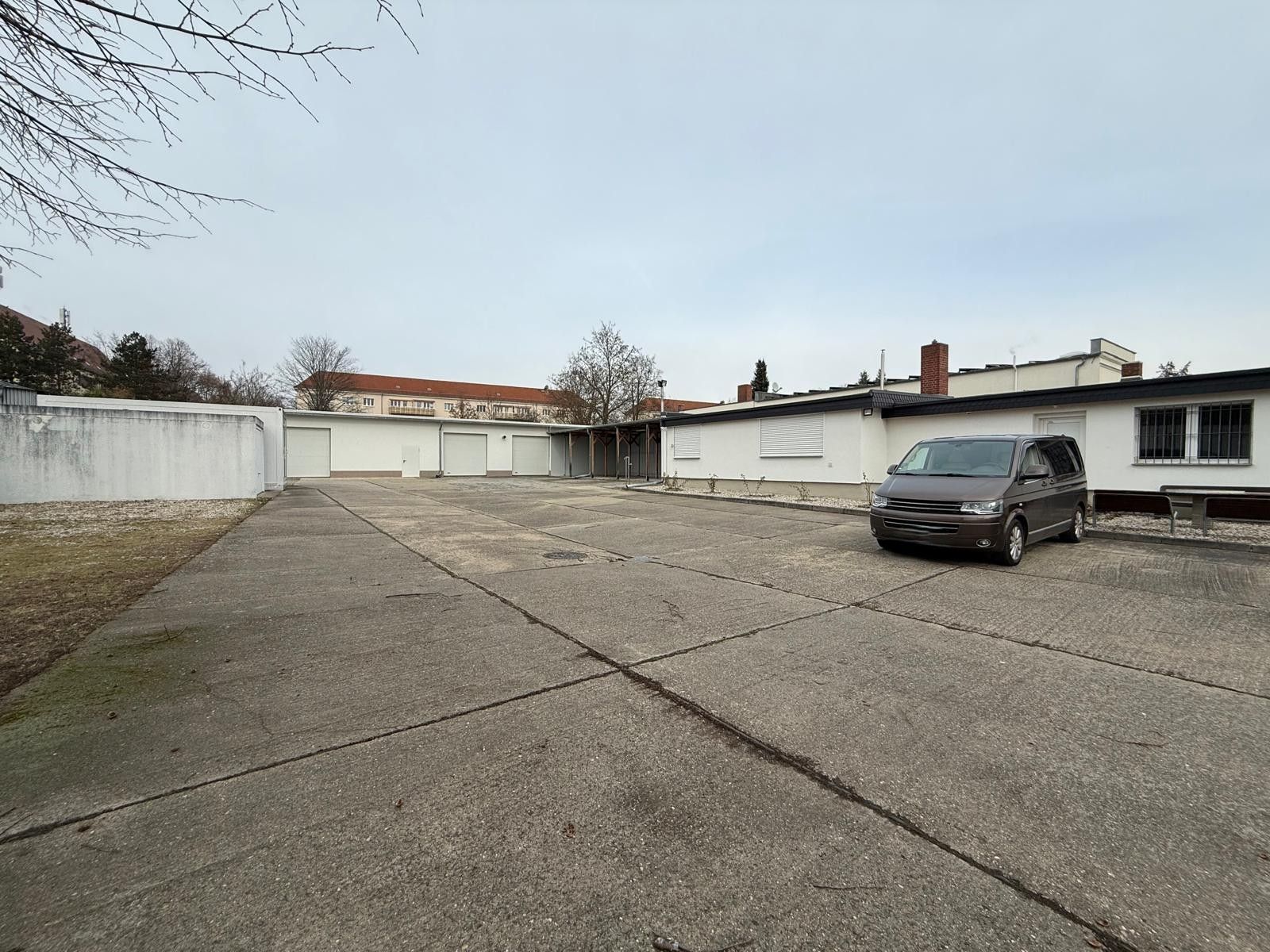Großer, leerer Hof mit einem geparkten Van und mehreren Garagen vor Wohnhäusern.