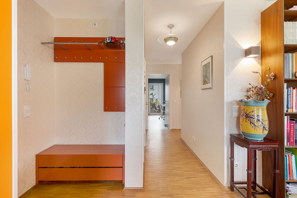 Heller Flur mit Garderobe, Holzboden, Bücherregal und Vase auf einem Tisch.