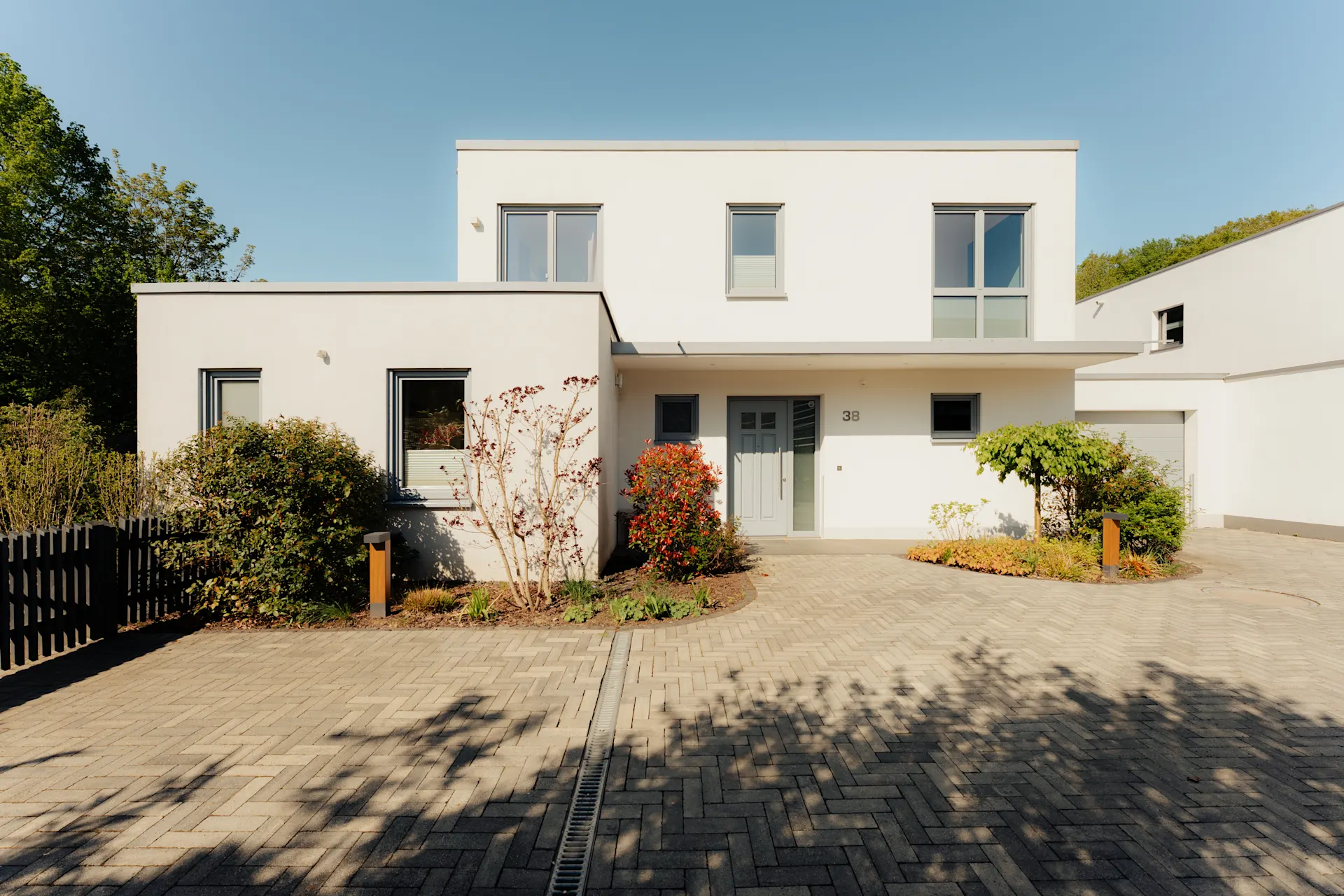 Modernes zweistöckiges Wohnhaus mit weißer Fassade, Vorgarten und gepflasterter Einfahrt.