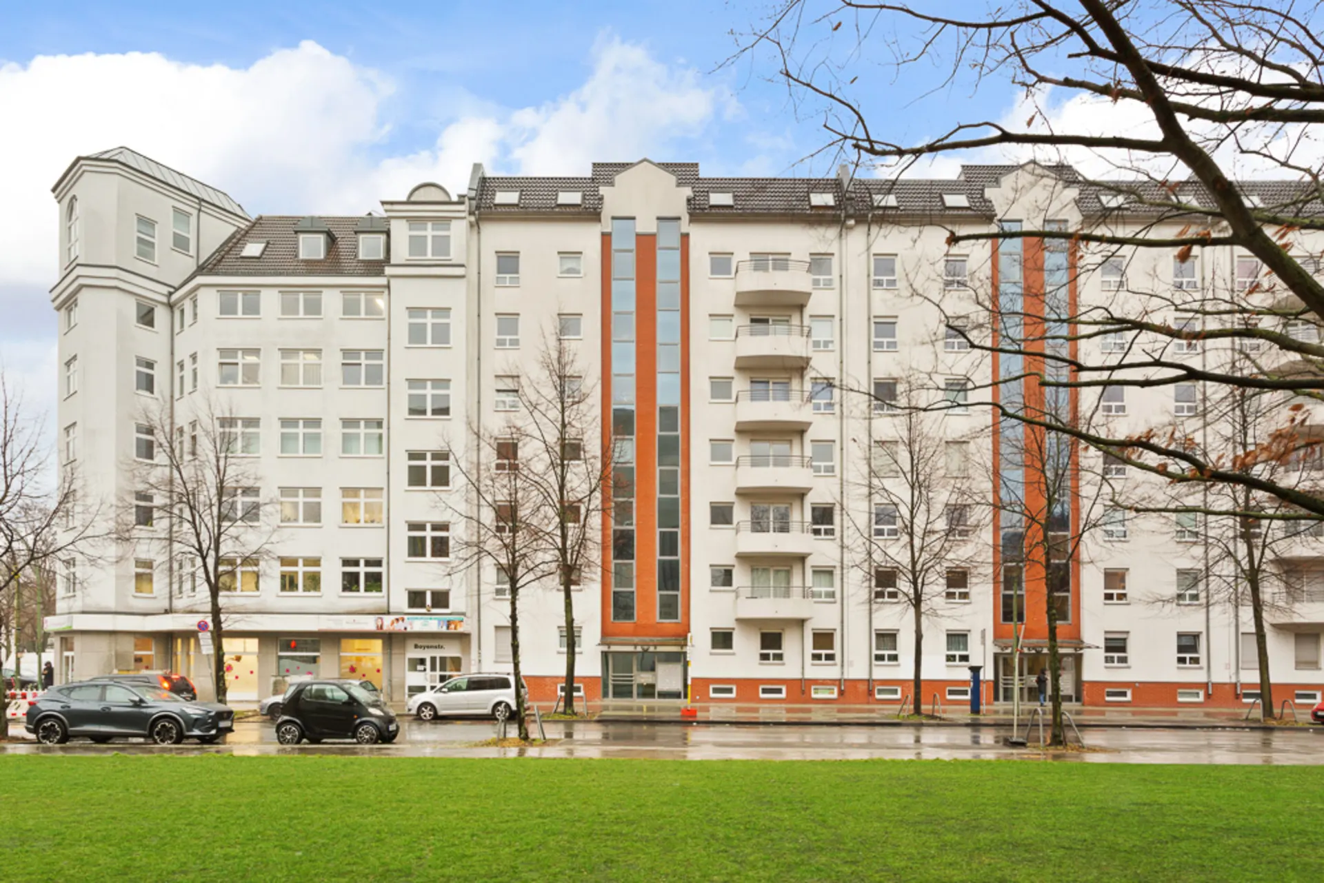 Mehrstöckiges Wohngebäude mit Balkonen, großen Fenstern und einigen geparkten Autos davor.