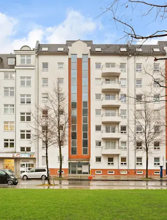 Mehrstöckiges Wohngebäude mit Balkonen, großen Fenstern und einigen geparkten Autos davor.