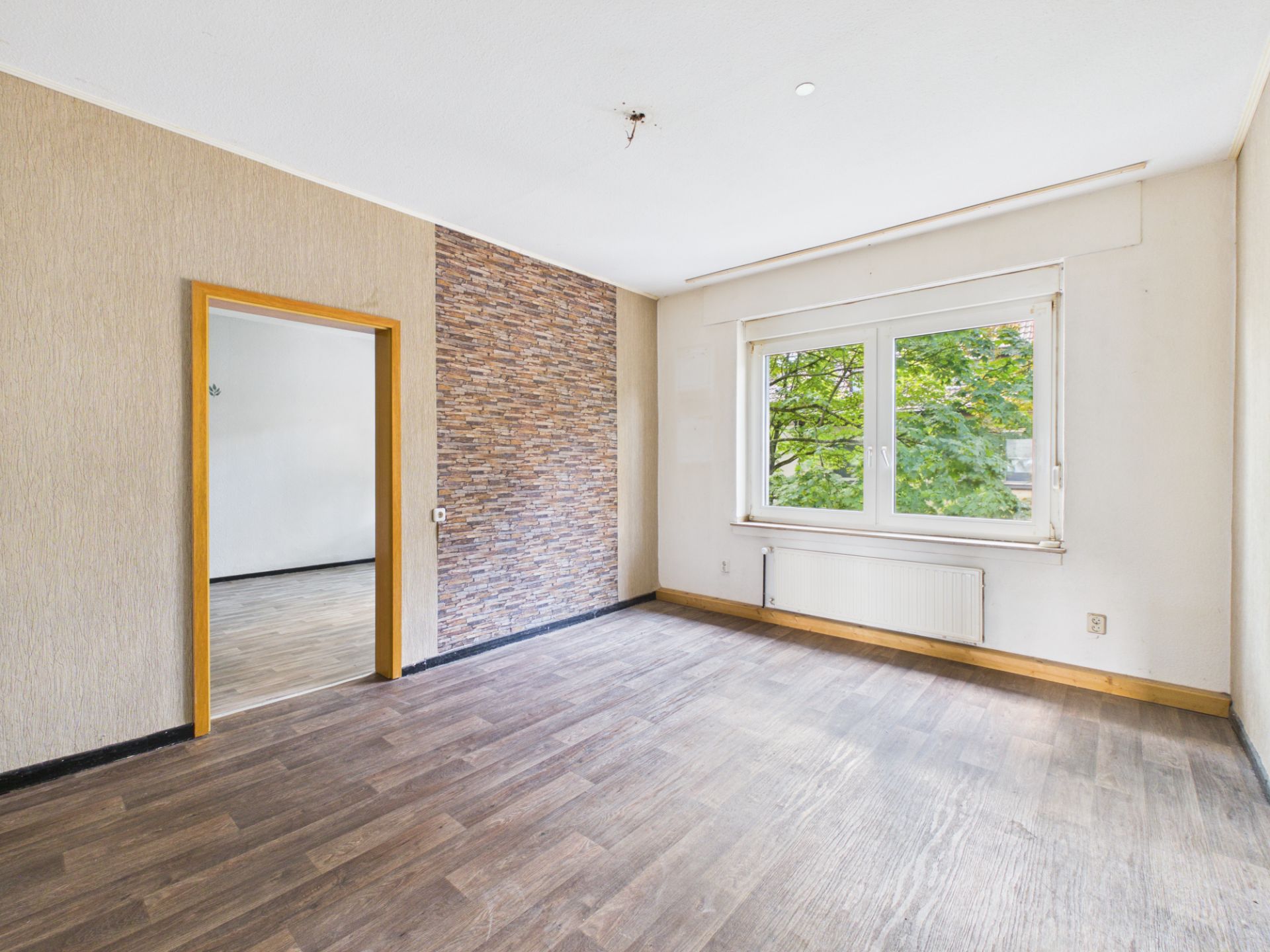Leerer Raum mit Holzfußboden, Fenster, Heizung und einer Wand mit Steintapete.
