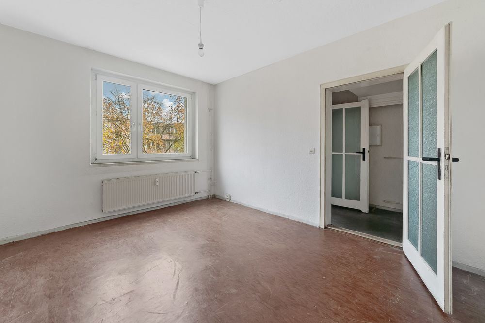 Leerer Raum mit braunem Boden, weißer Wand, Fenster und offener Tür.