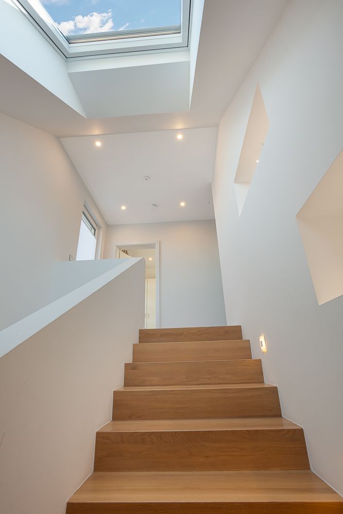 Holztreppe in modernem Flur mit Dachfenster und weißen Wänden.