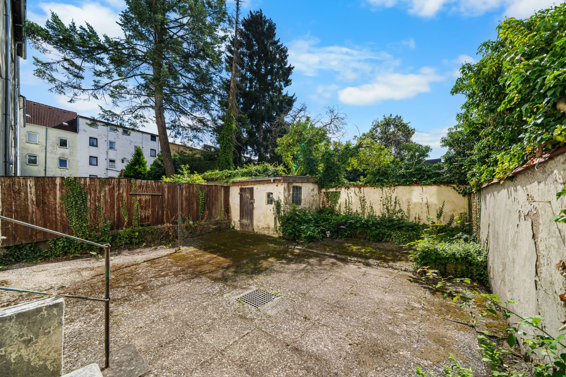 Blick auf einen Hof mit Betonboden, alten Mauern und einigen Pflanzen an den Rändern.