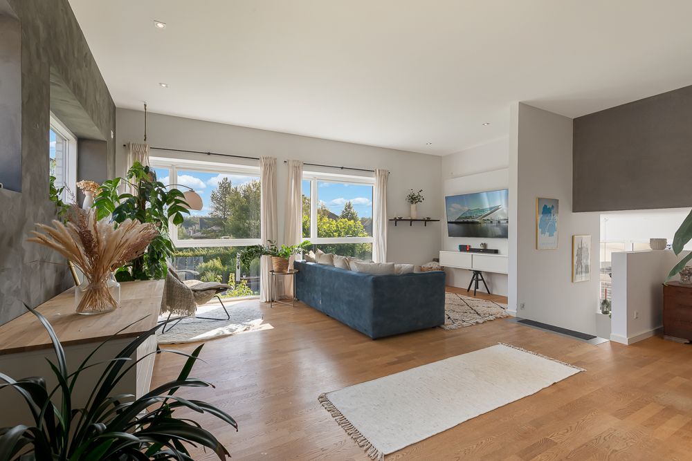 Helles Wohnzimmer mit Holzfußboden, Sofa, großen Fenstern und Zimmerpflanzen.