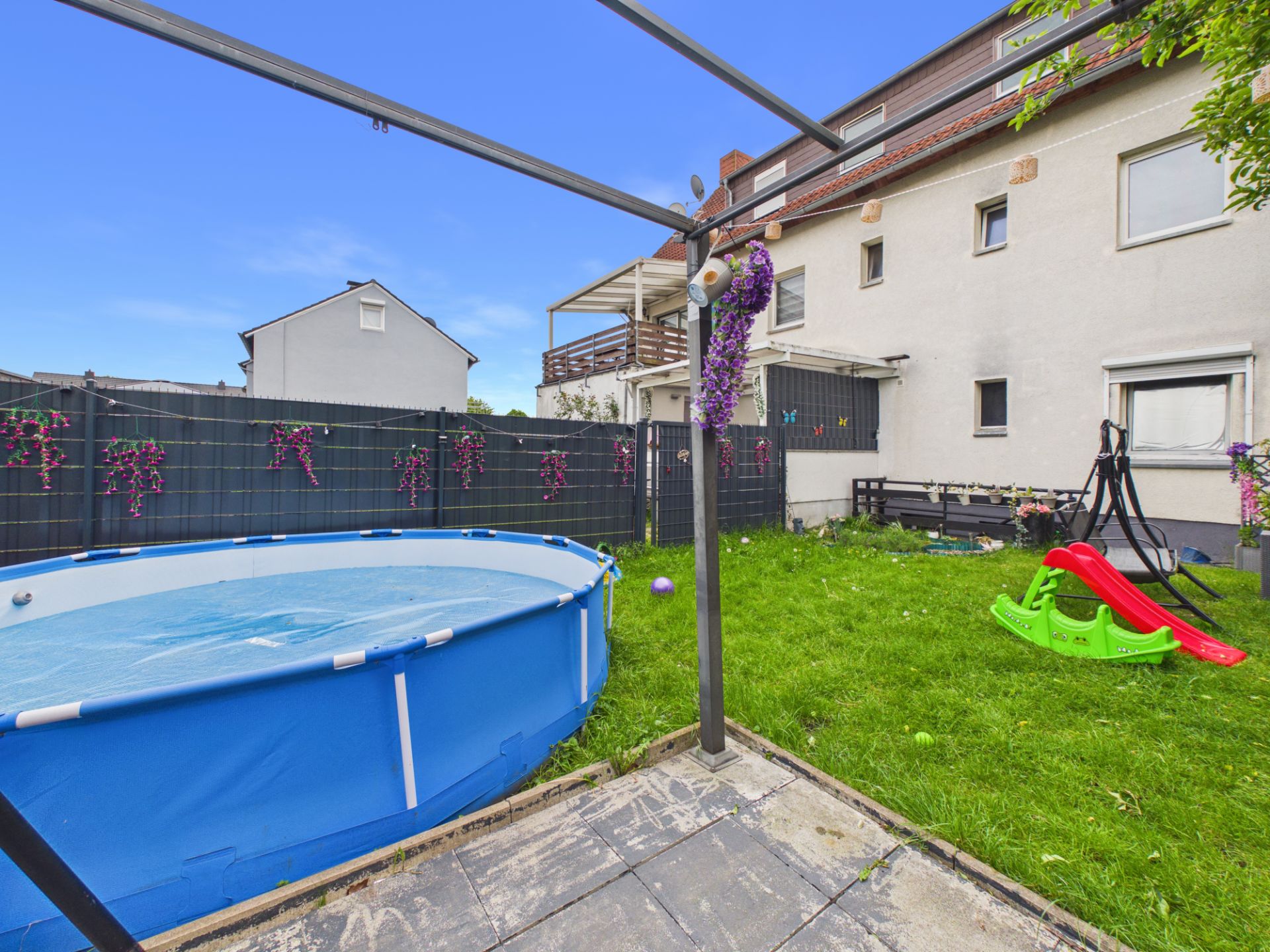 Garten mit aufblasbarem Pool, Rutsche, Schaukel und Wiese hinter einem Wohnhaus.