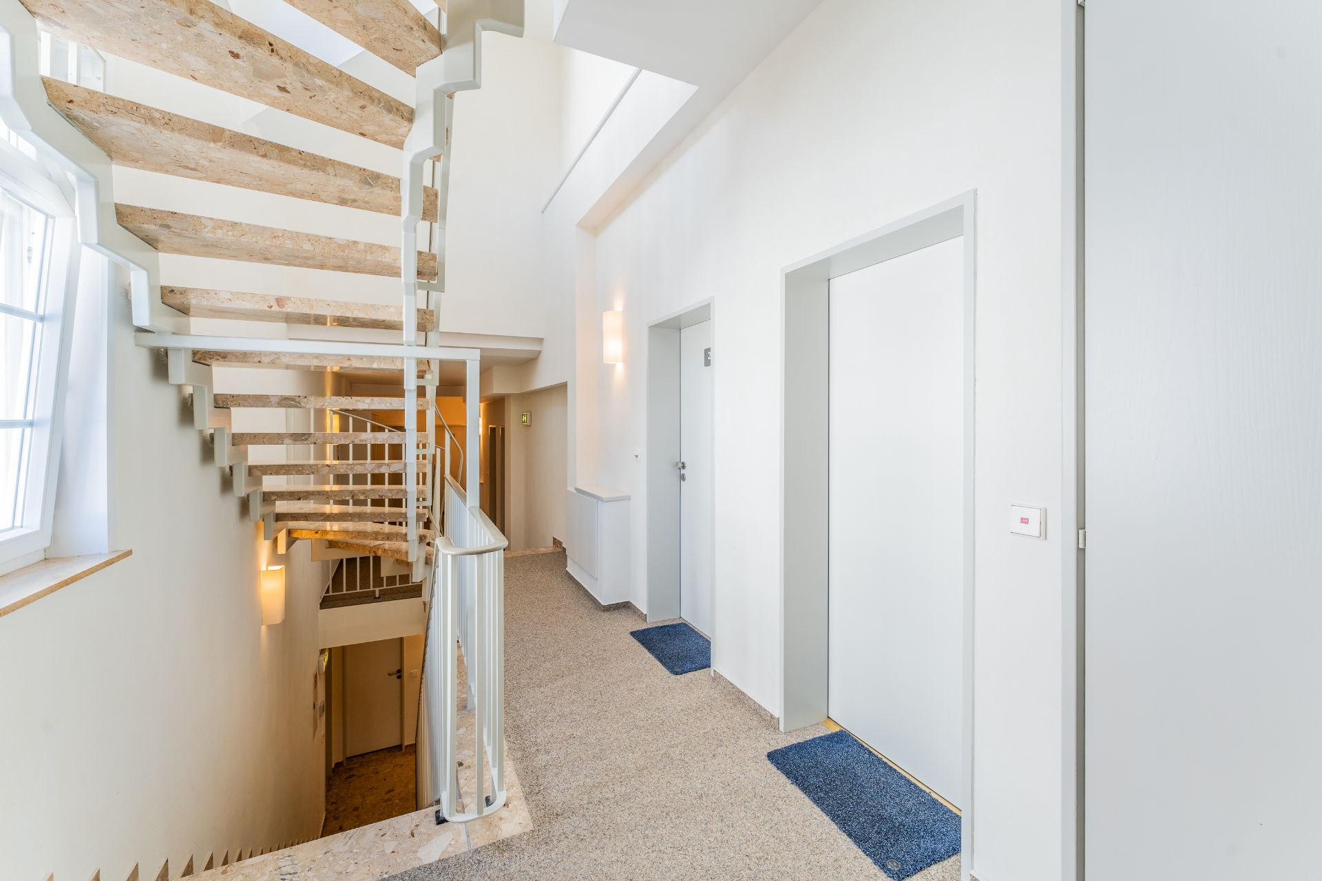 Helles Treppenhaus mit modernen Holztreppen und hellen Wohnungstüren im Wohngebäude.