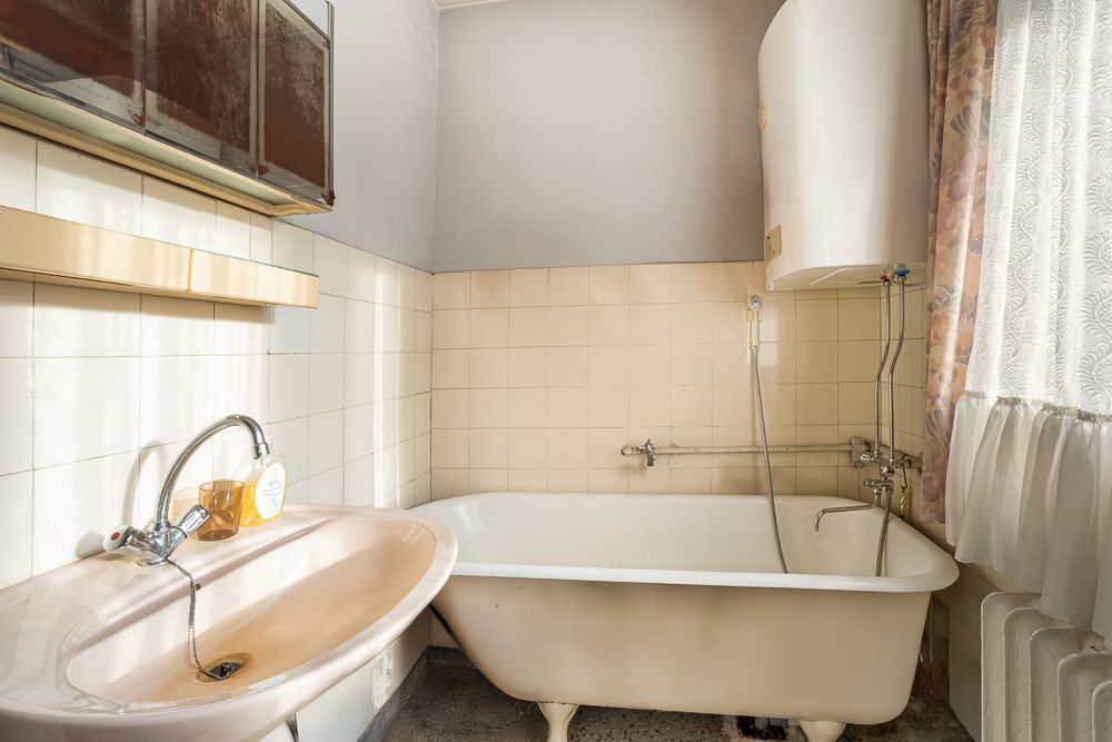 Altes Badezimmer mit Badewanne, Waschbecken und großem Fenster mit Vorhang.
