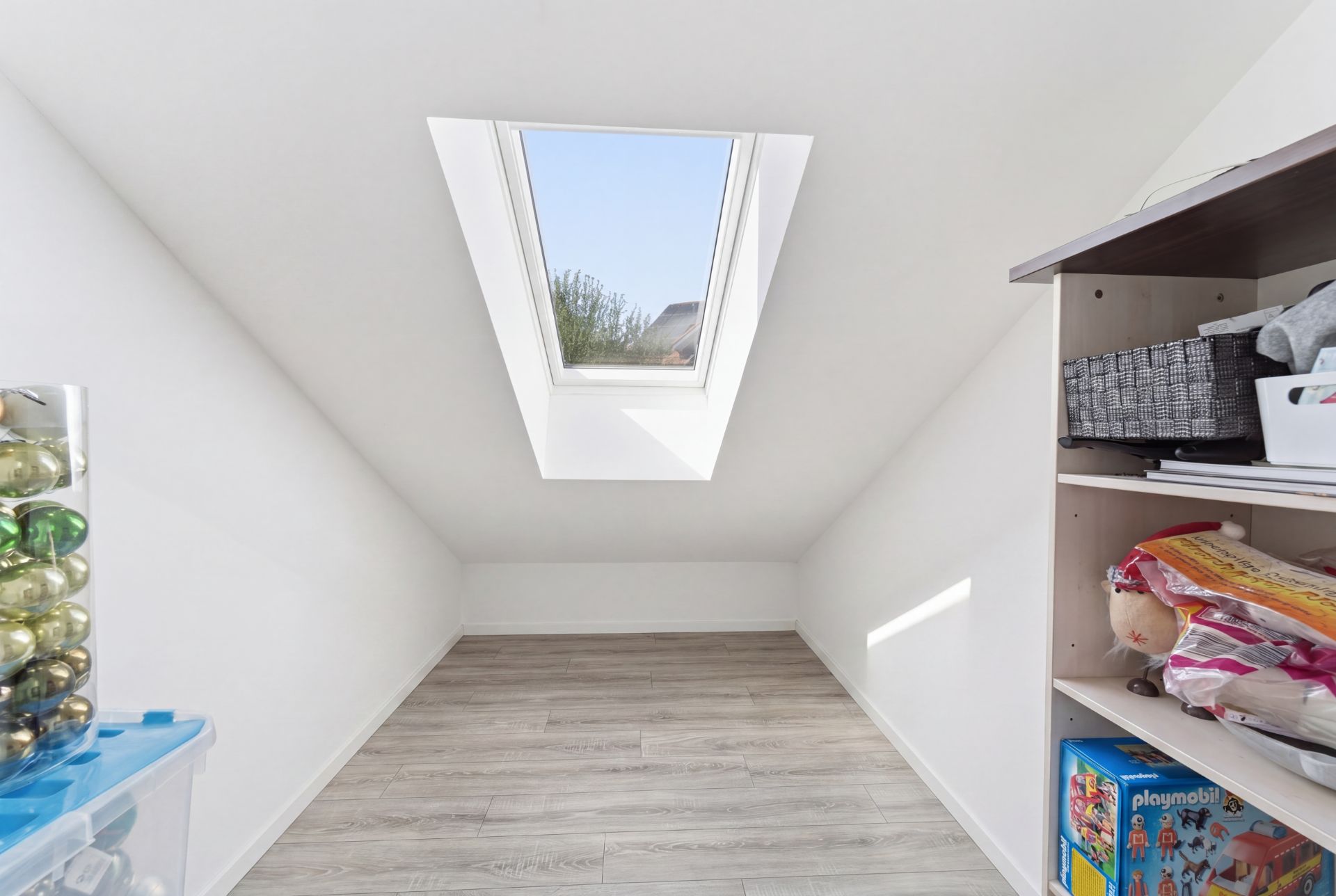 Heller Raum mit Dachfenster, Holzfußboden und Regal mit Spielsachen an der Seite.