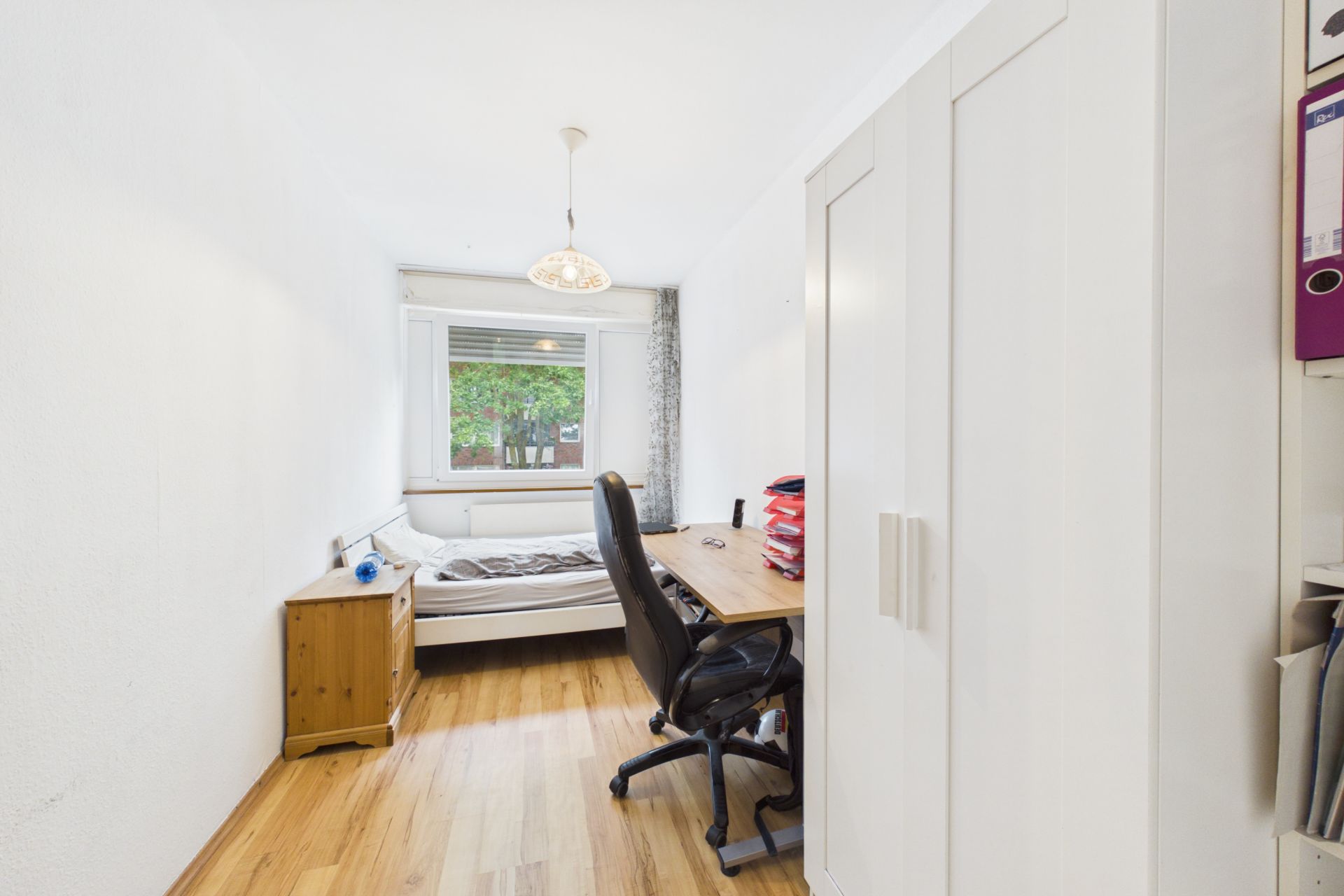 Helles Schlafzimmer mit Bett, Schreibtisch, Stuhl, Kleiderschrank und Fenster.