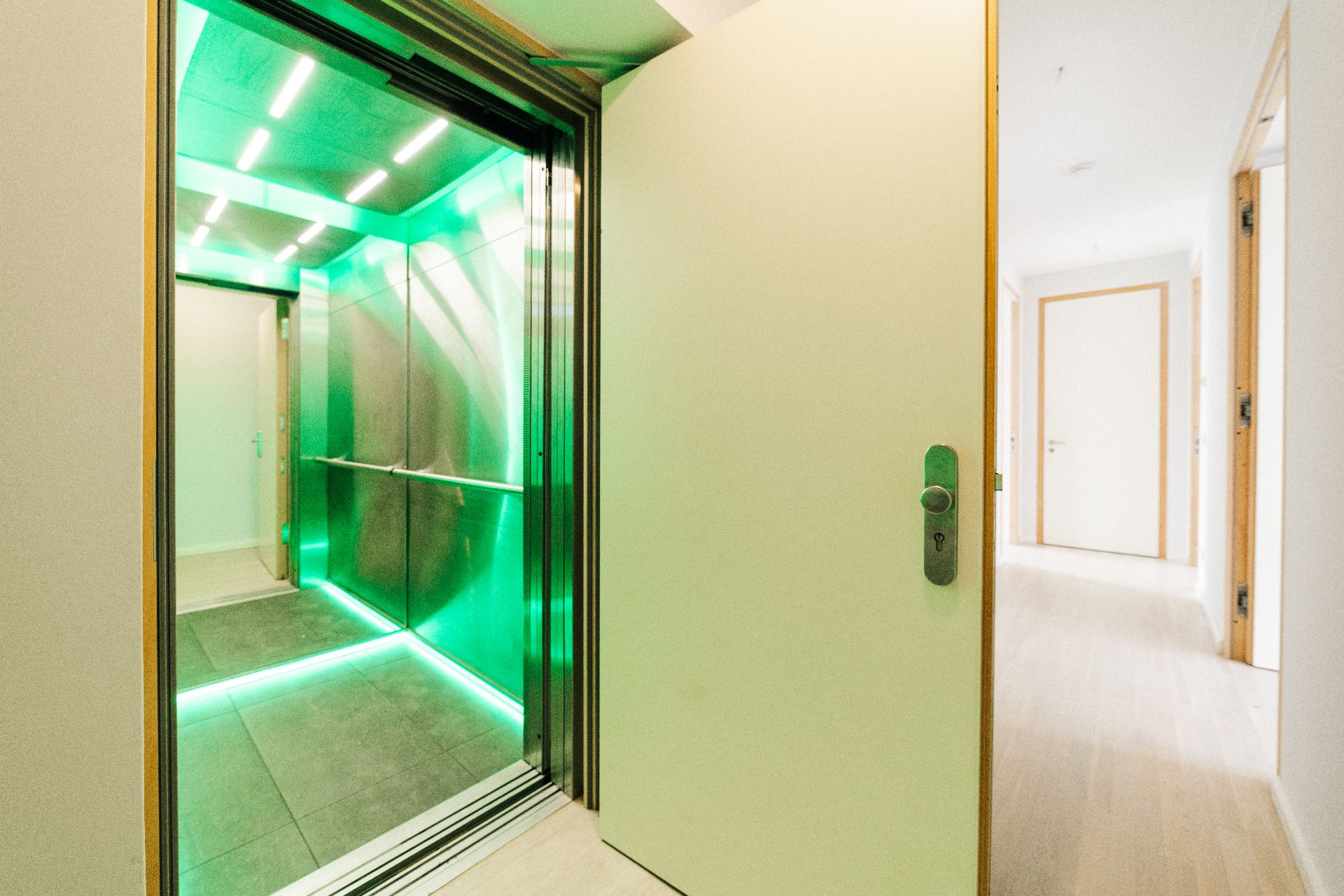 Offene Wohnungstür mit Blick auf einen beleuchteten Aufzug mit grüner Innenbeleuchtung.