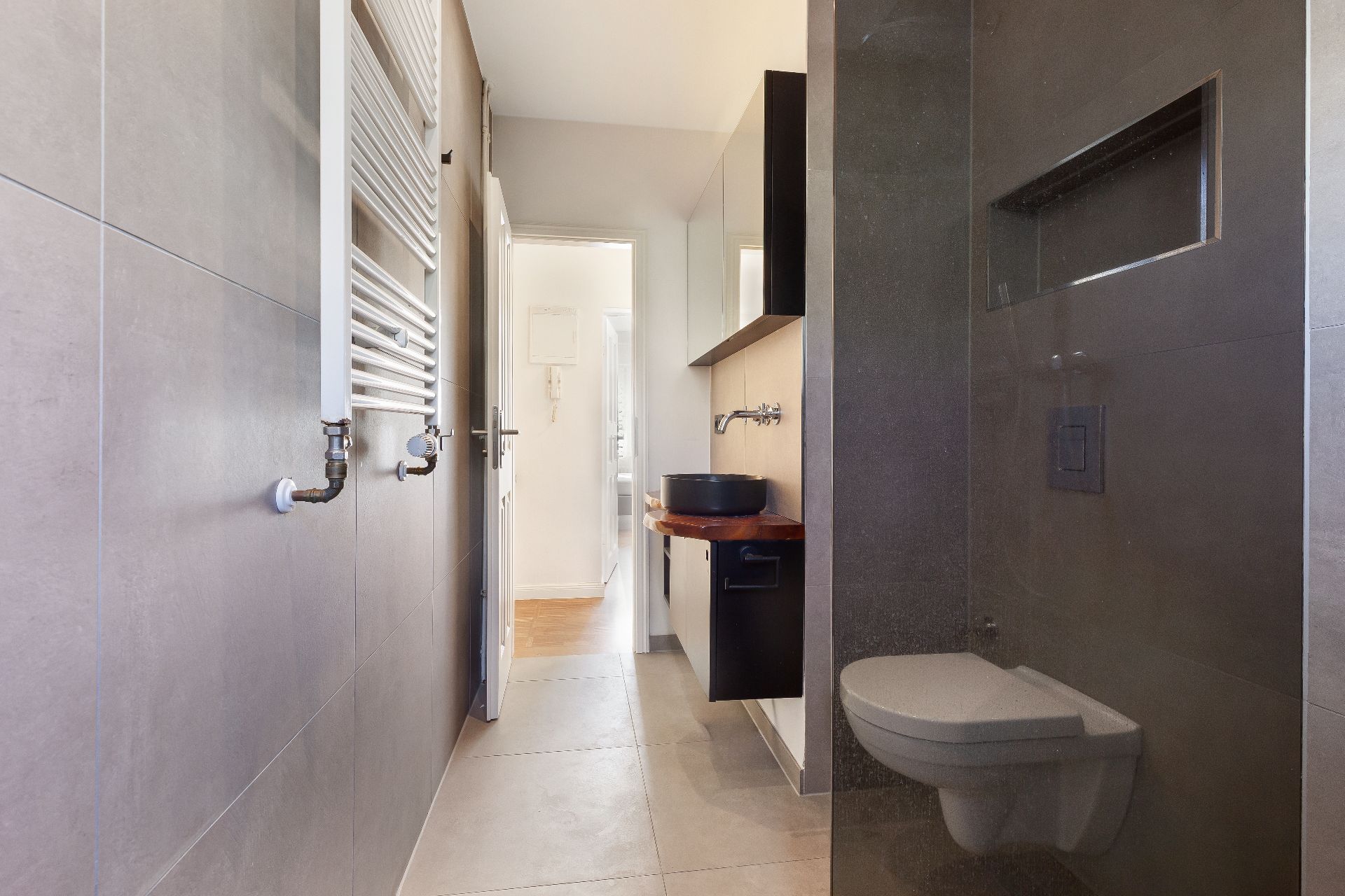 Modernes Badezimmer mit Wand-WC, dunklem Waschbecken und Handtuchheizkörper.