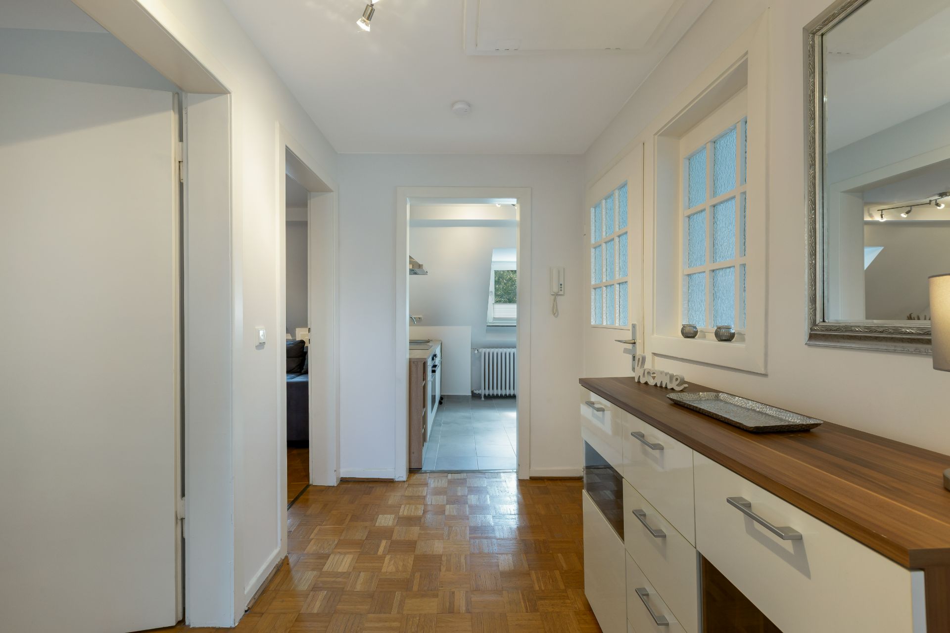 Heller Flur mit Holzkommode und Spiegel, Blick in eine Küche mit Fenster.
