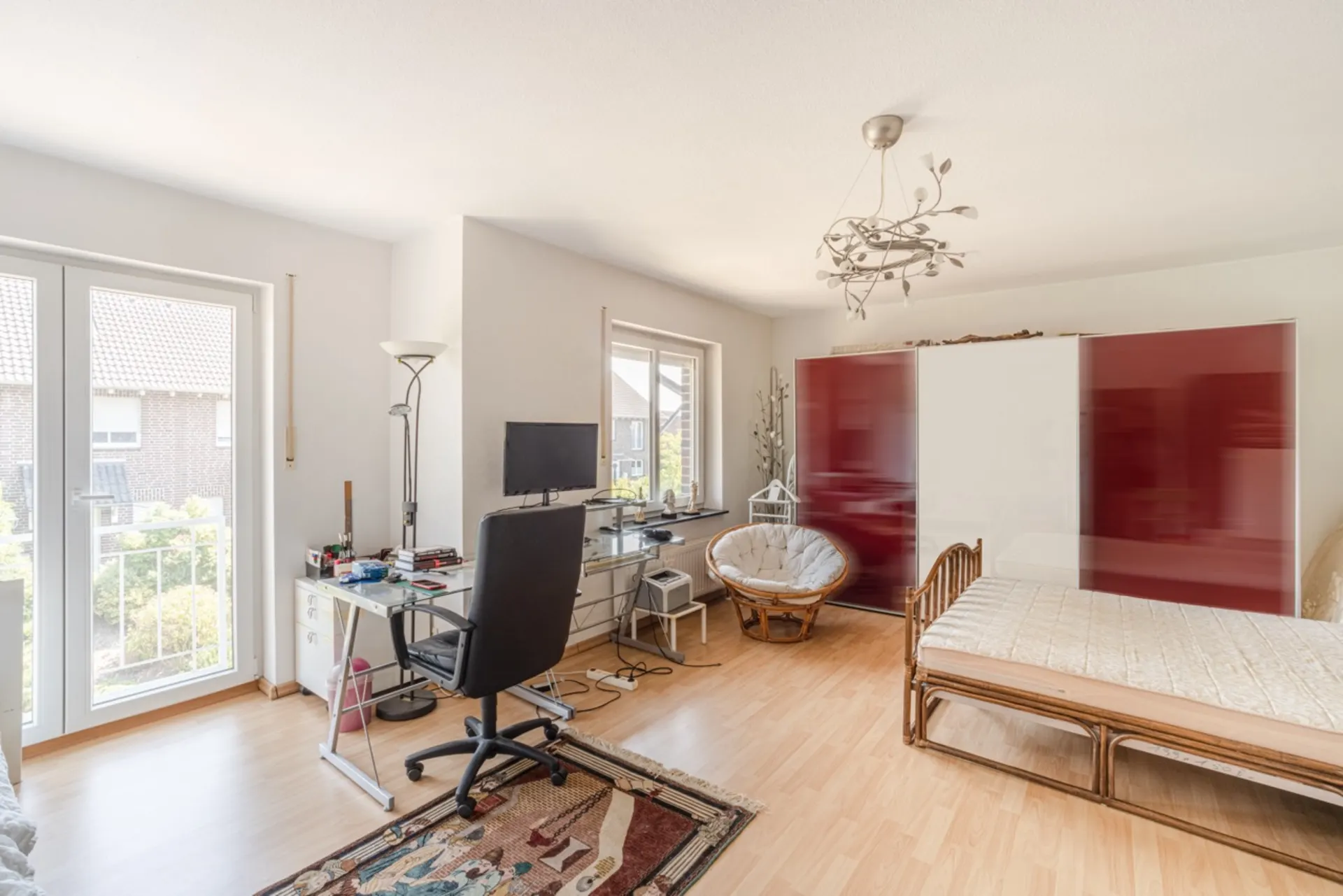 Helles Zimmer mit Schreibtisch, Stuhl, Einzelbett, großem Kleiderschrank und Balkonzugang.