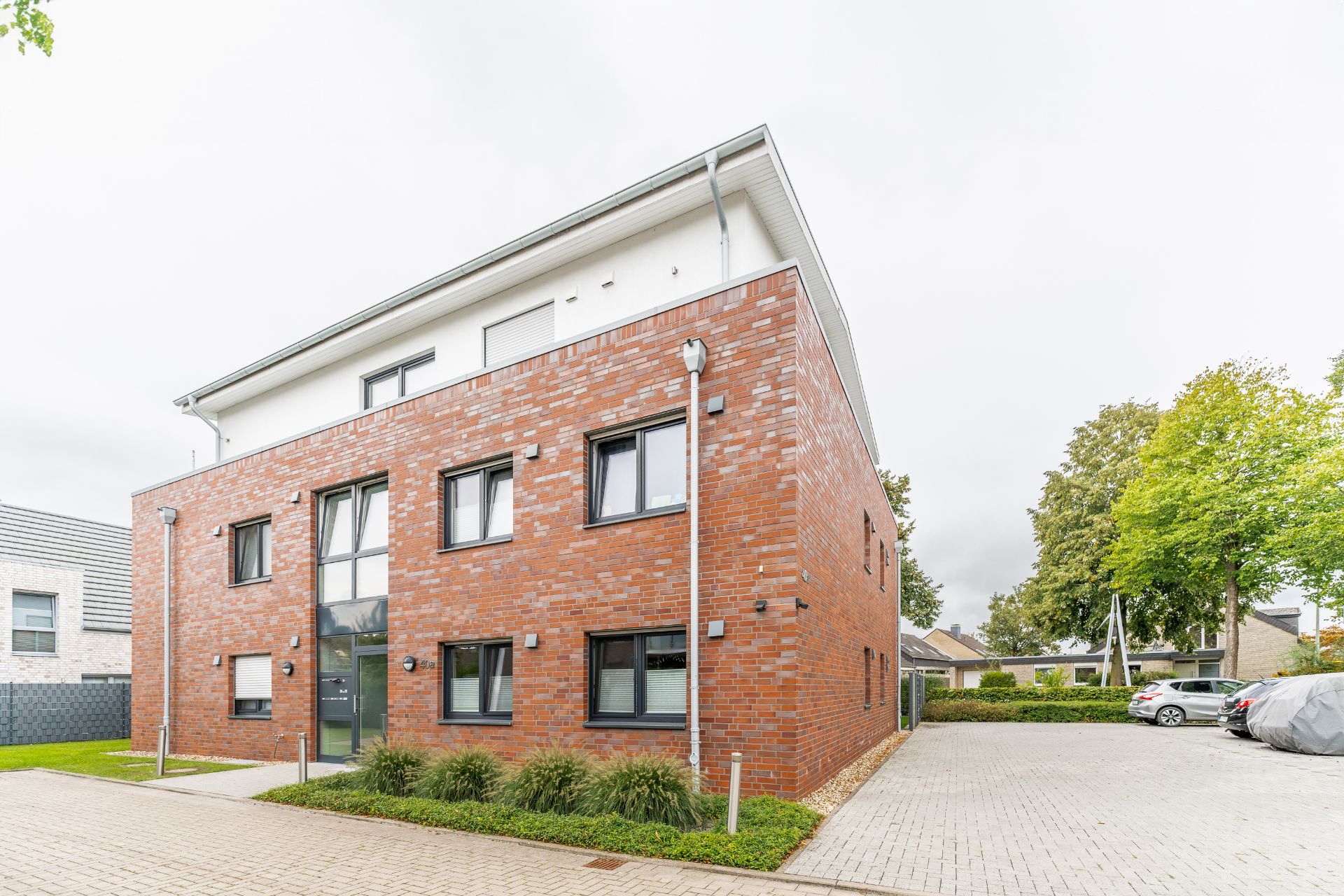 Modernes, dreistöckiges Wohngebäude mit roter Backsteinfassade und großen Fenstern.