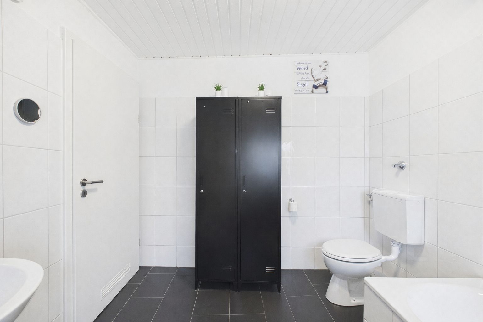 Helles Badezimmer mit schwarzem Schrank, Toilette und weißen Fliesen.