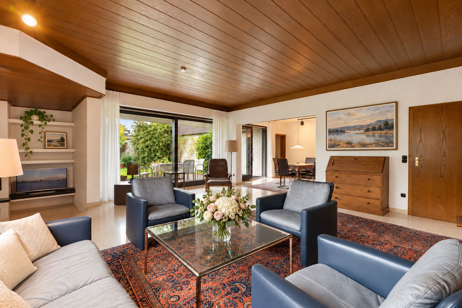Helles Wohnzimmer mit Sofas, Glastisch, Teppich und Zugang zum Garten.