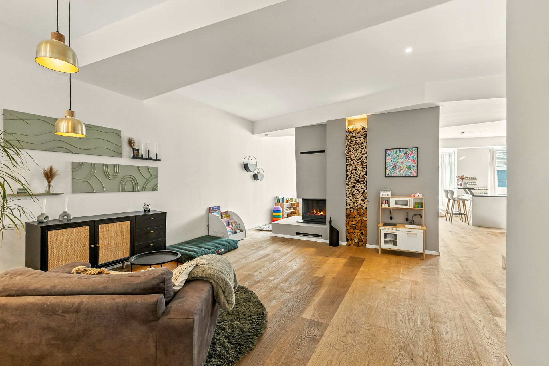 Modernes Wohnzimmer mit Holzfußboden, Kamin, Spielzeug, Sofa und Essbereich im Hintergrund.