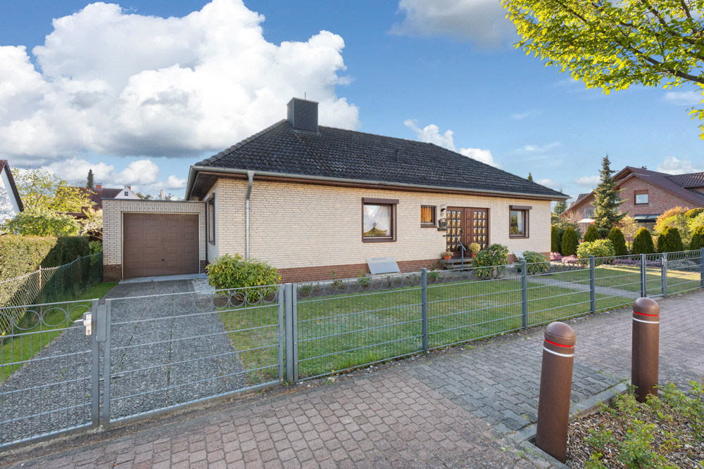 Einfamilienhaus mit Garage, Vorgarten und Metallzaun bei sonnigem Wetter.