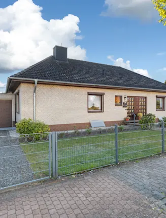 Einfamilienhaus mit Garage, Vorgarten und Metallzaun bei sonnigem Wetter.