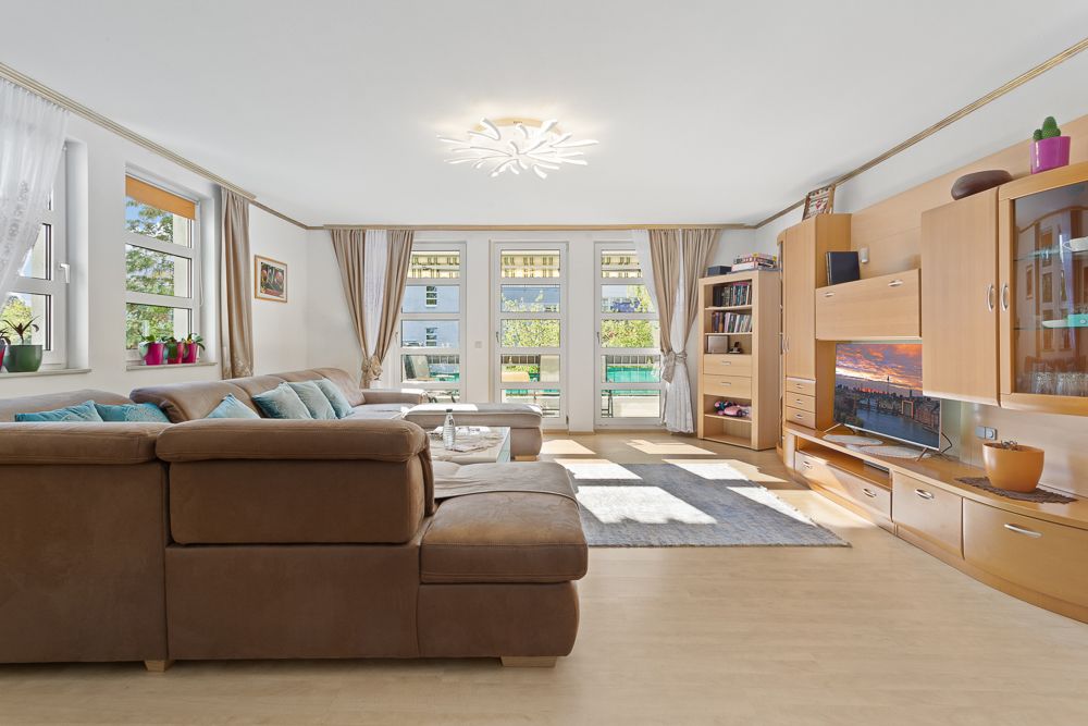 Helles Wohnzimmer mit braunem Sofa, Holzregalen, Teppich und großen Fenstern.