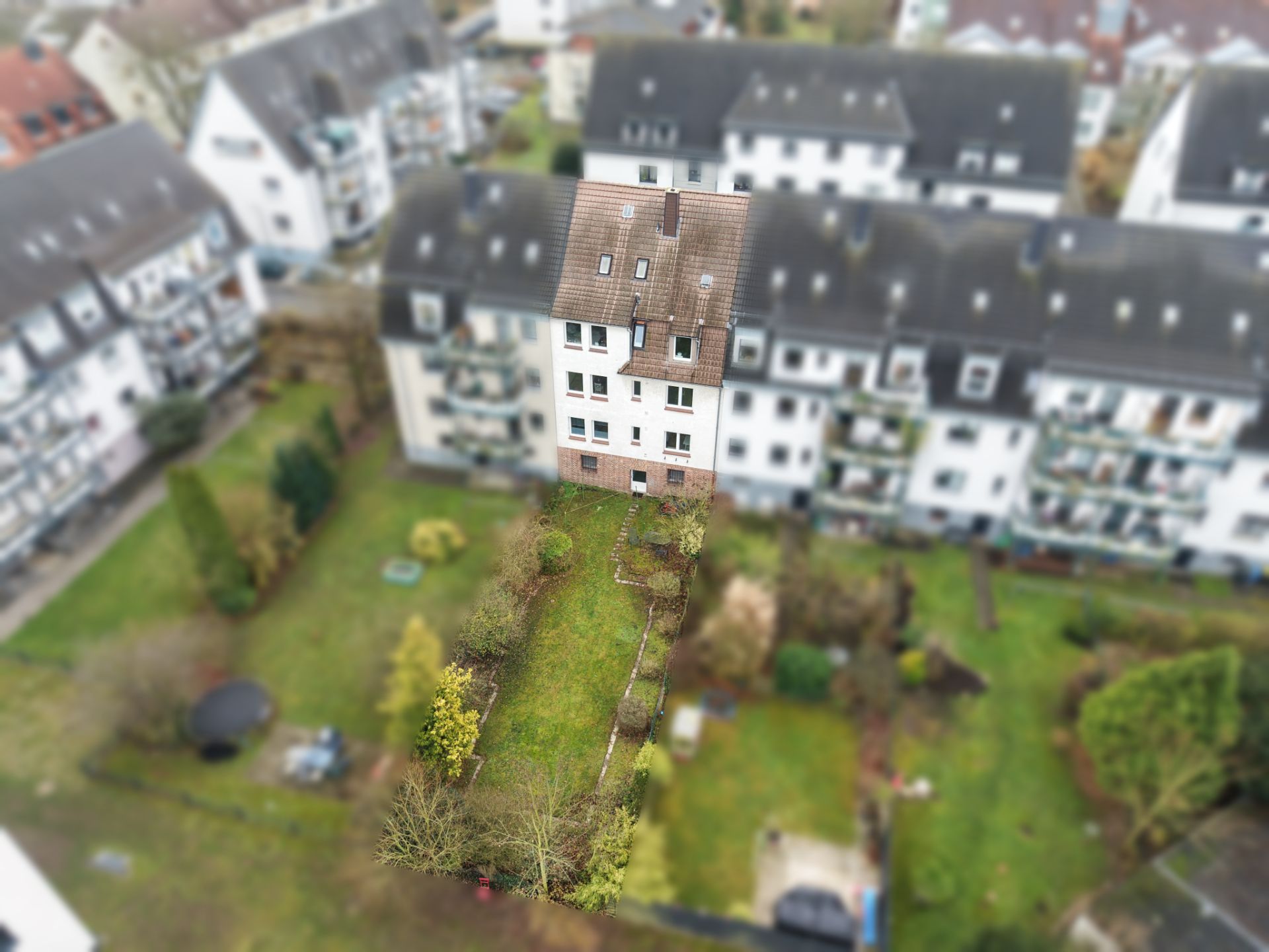 Mehrfamilienhaus mit Garten und umliegenden Wohngebäuden, aus der Vogelperspektive aufgenommen.
