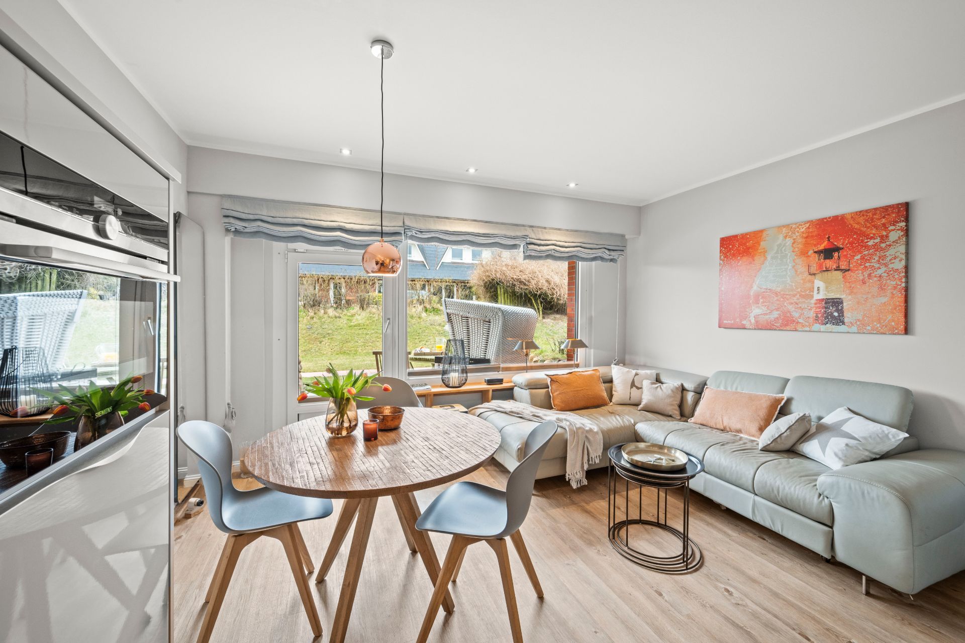 Helles Wohnzimmer mit runder Essgruppe, Ecksofa und großem Fenster mit Blick in den Garten.