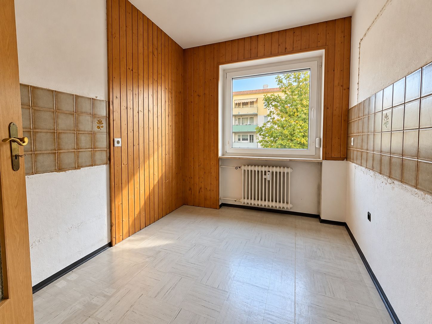 Leerer Raum mit Holzverkleidung, Fenster, Heizkörper und Fliesen an den Wänden.