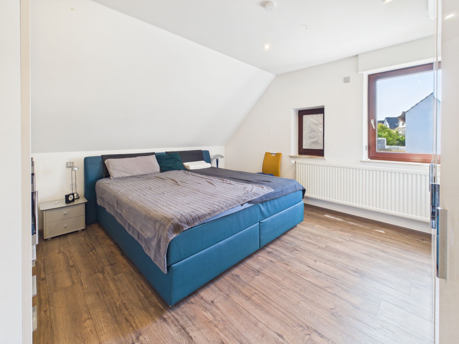 Helles Schlafzimmer mit Doppelbett, Nachttischen und großem Fenster auf Holzfußboden.