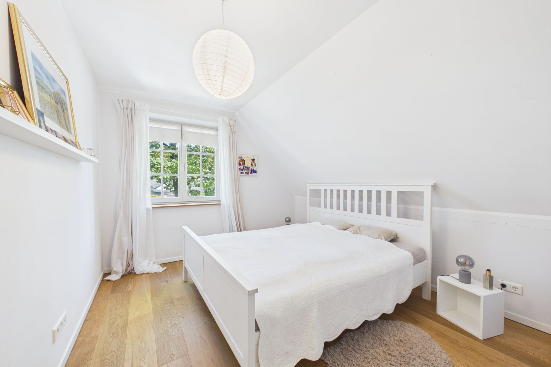 Helles Schlafzimmer mit weißem Bett, Holzfußboden und großem Fenster.