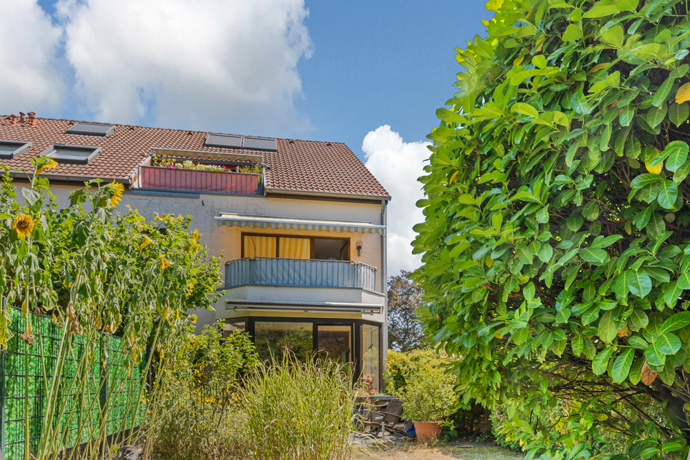 Wohnhaus mit Balkon, Garten, Sonnenblumen und großen Büschen im Vordergrund.