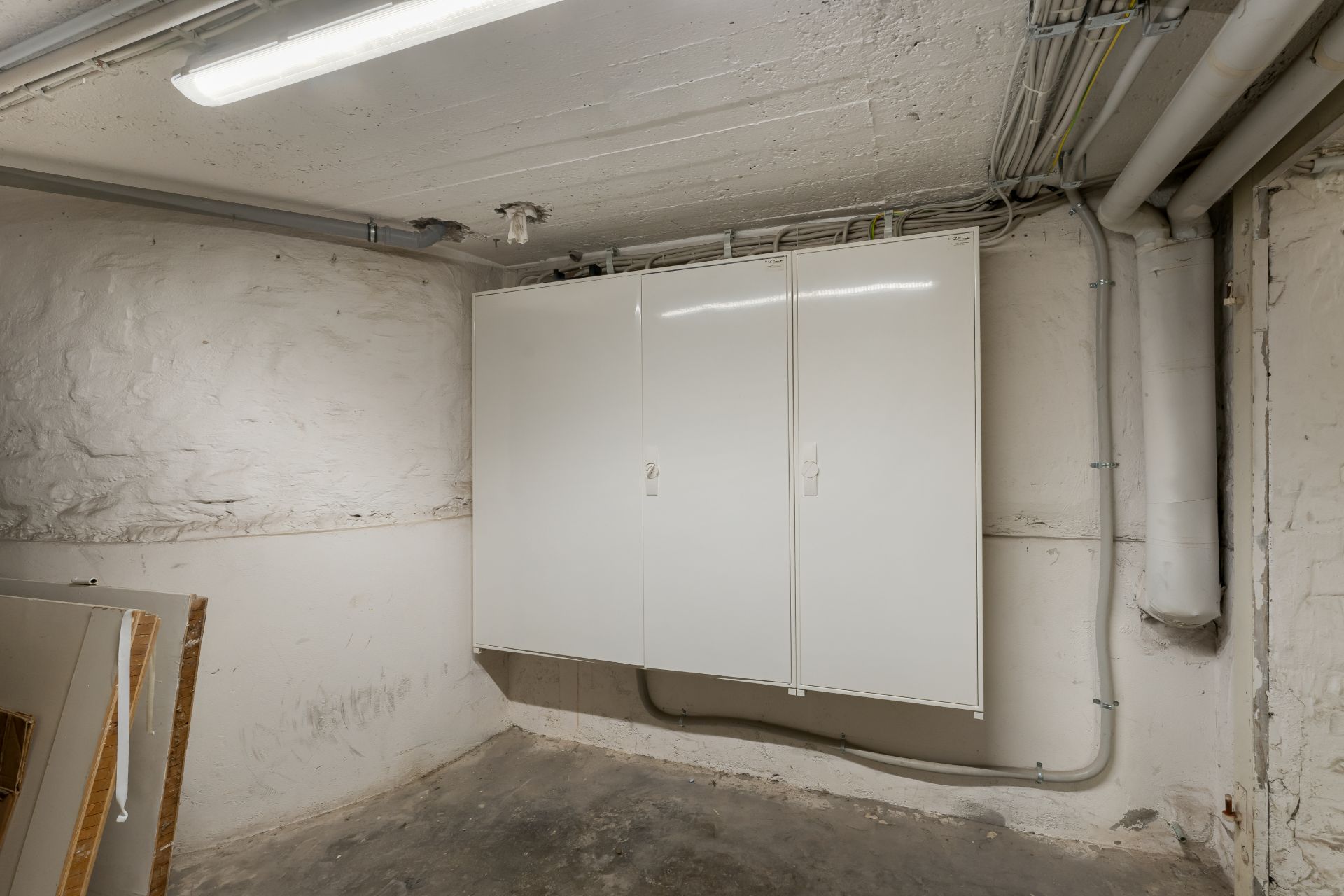 Kellerraum mit weißen Wandschränken und sichtbaren Rohren an der Decke.