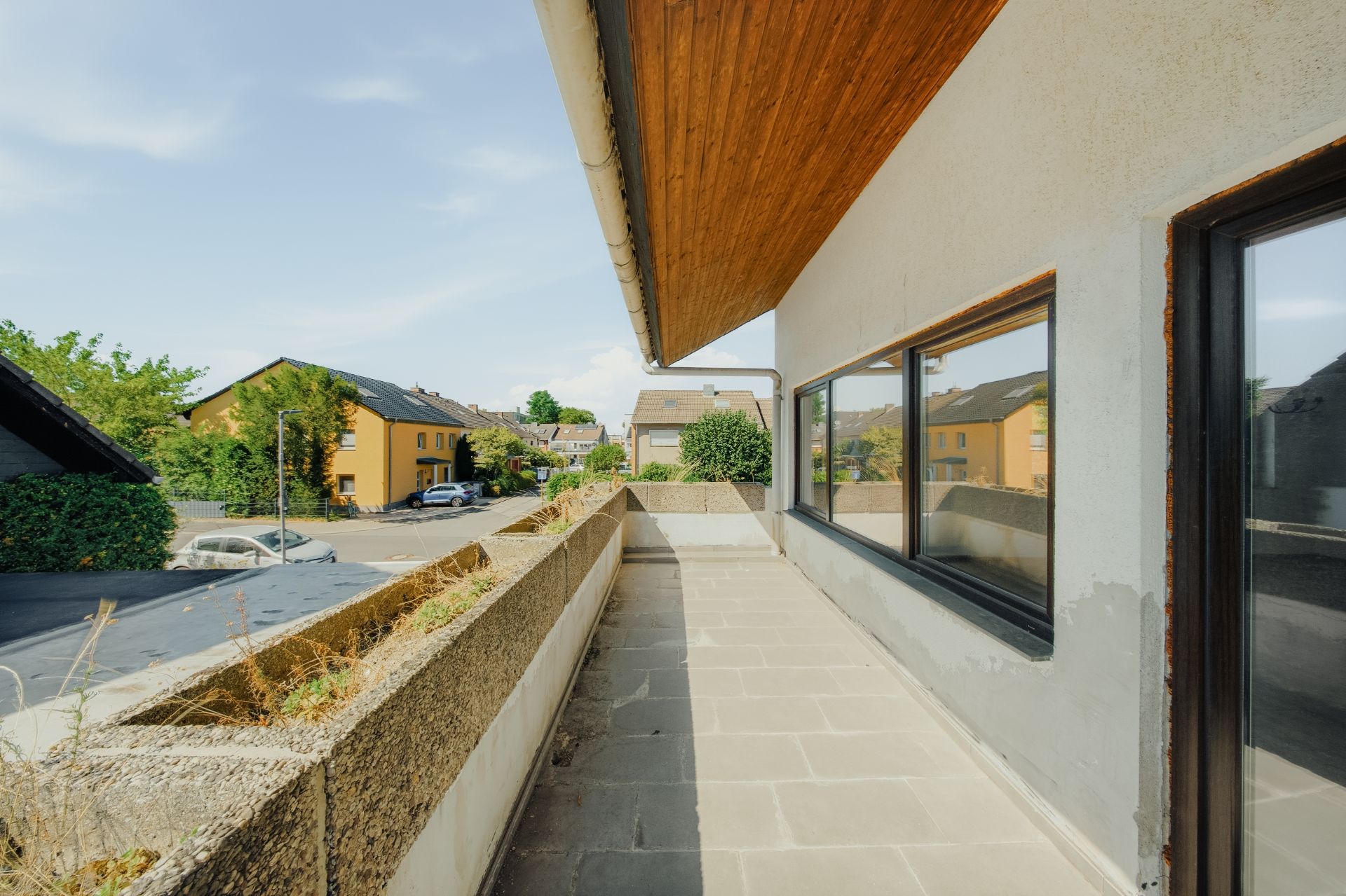 Geräumiger Balkon mit Steinboden und Ausblick auf Wohnhäuser und Straße.