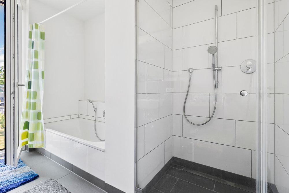 Modernes Badezimmer mit Dusche, Badewanne und grün-gemusterter Duschvorhang.