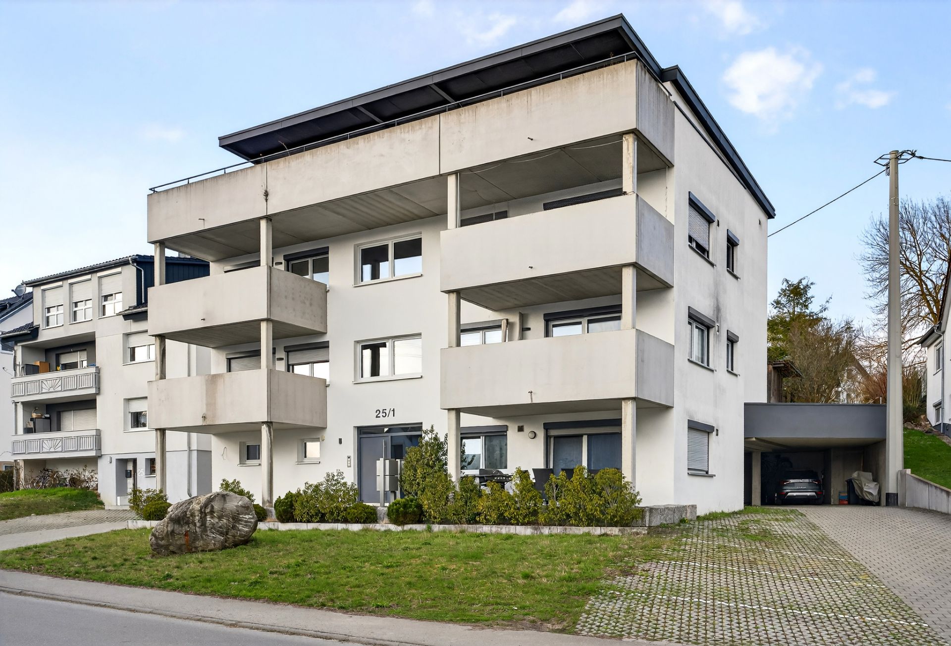 Modernes, dreistöckiges Wohngebäude mit großen Balkonen und begrüntem Vorgarten.