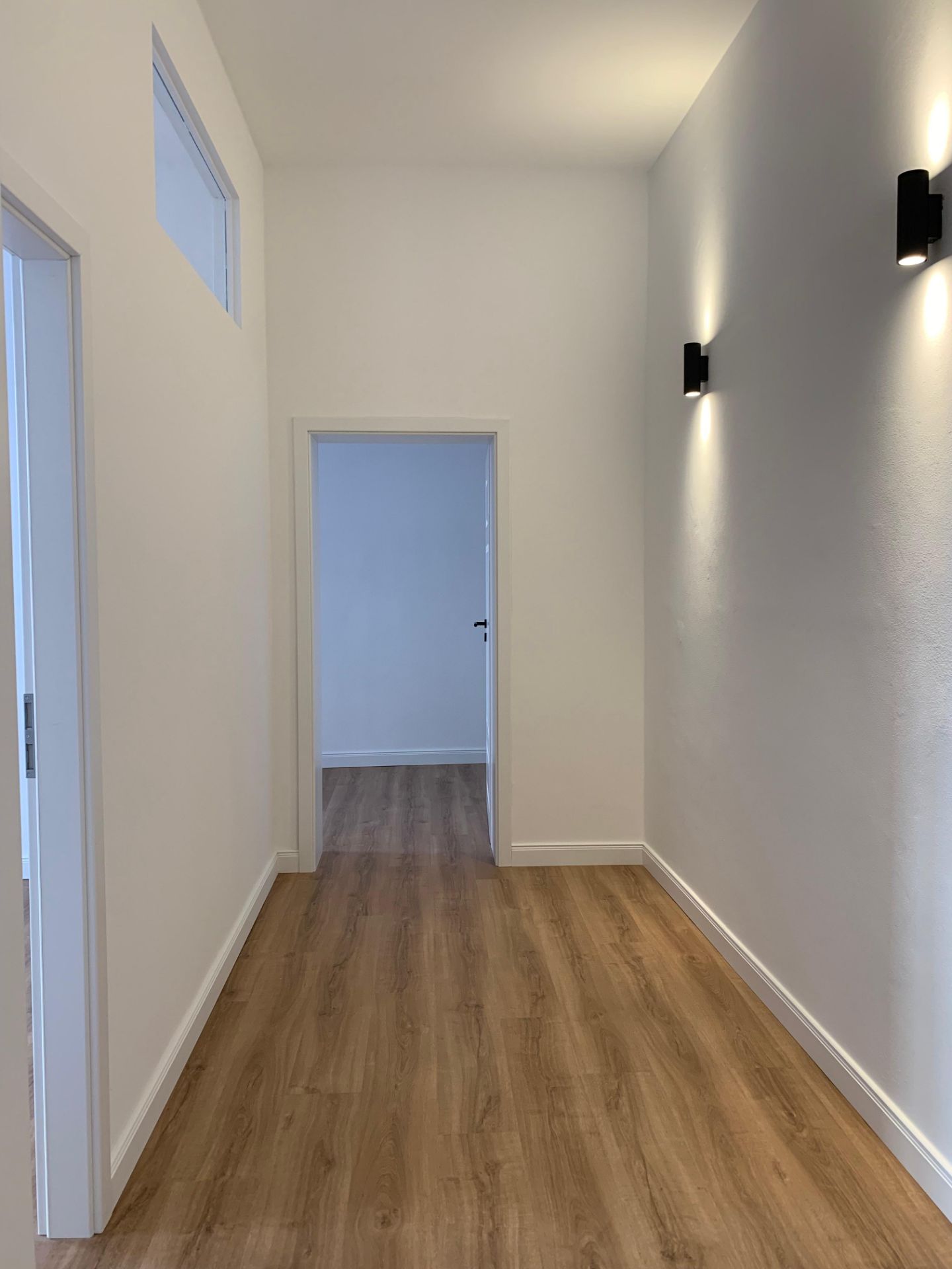 Heller Flur mit Holzfußboden, weißen Wänden und modernen Wandlampen.