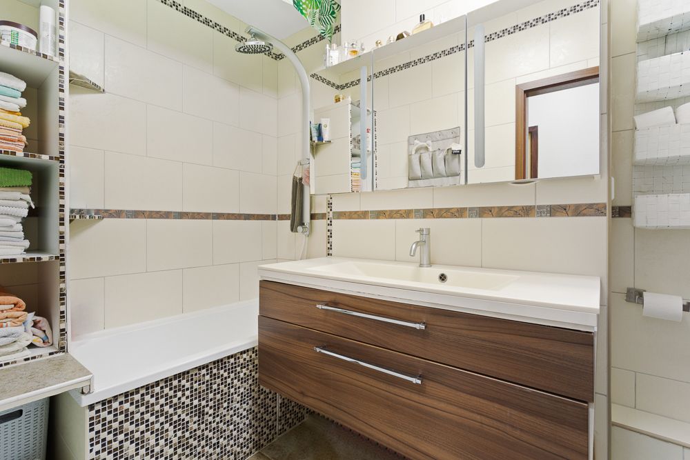 Modernes Badezimmer mit Badewanne, Waschtisch aus Holz, Spiegel und Regalen mit Handtüchern.