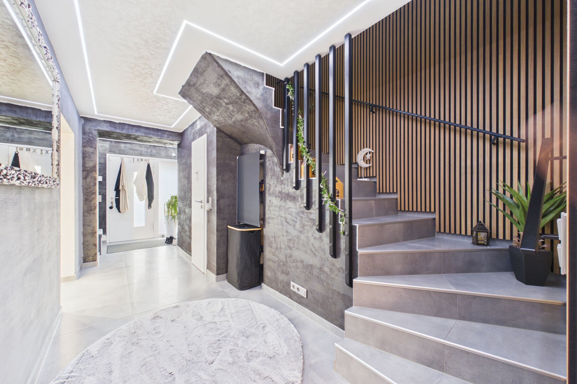 Moderner Eingangsbereich mit Treppe, grauem Boden, Holzwand und Pflanzen.