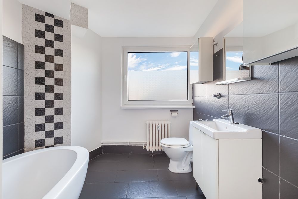 Modernes Badezimmer mit Badewanne, Waschbecken, Toilette und großem Fenster.